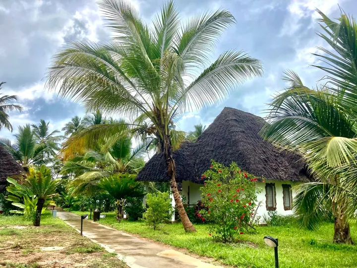 Kryty strzechą bungalow wśród palm w hotelu na Zanzibarze